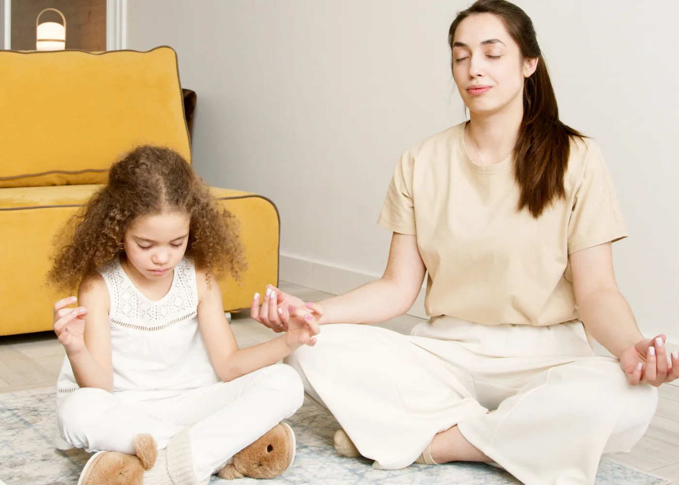 Una madre e una bambina meditano insieme tenendosi per mano in una stanza luminosa