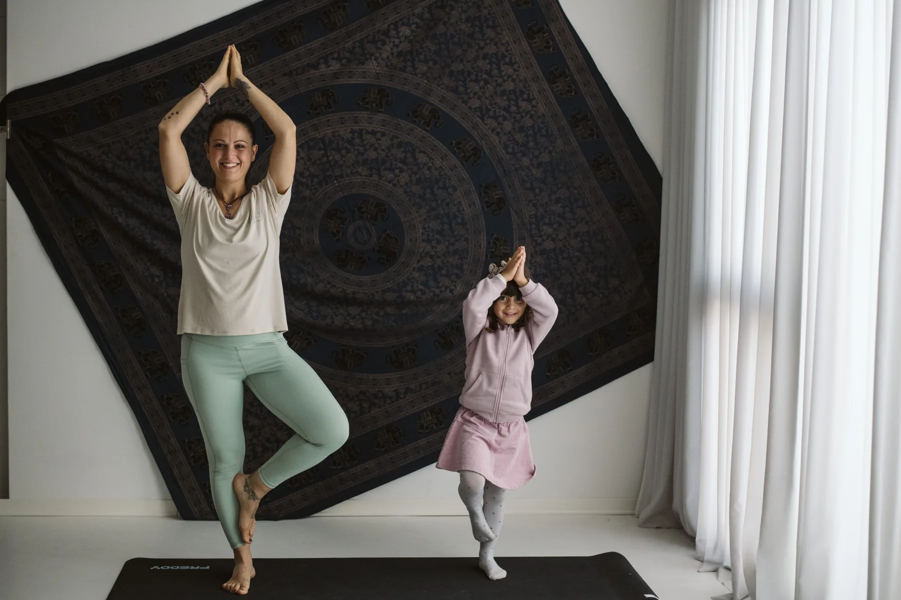 Una madre e una bambina sorridono mentre provano insieme una posizione di equilibrio in casa